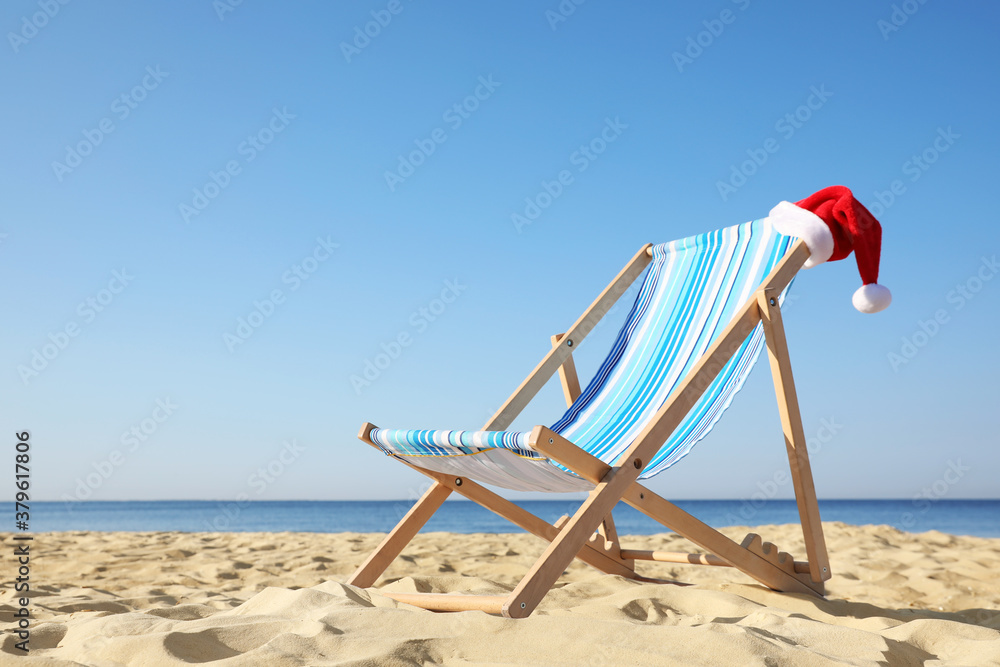 Deck chair with Santa Claus hat on sandy beach. Christmas vacation Deck chair with Santa Claus hat on sandy beach. Christmas vacation