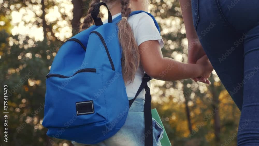 mom and daughter go to school. happy family education concept. schoolgirl with mom and daughter go hand in hand to school on footpath in lifestyle the park. little girl with a briefcase time to study