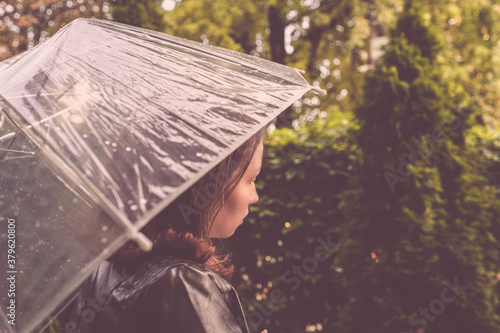 Autumn. Lonely redhead girl under a transparent umbrella with rain drops walking in a park, garden. Rainy day landscape. Vintage Toned