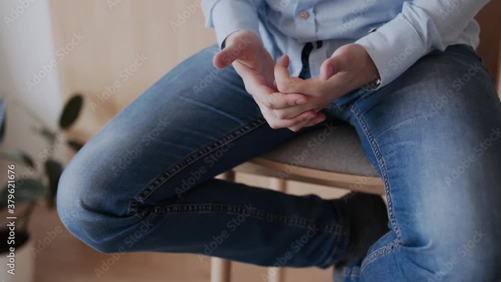 A man in a blue shirt and jeans sits on a wooden bar stool and gestures with his hands, close-up of fingers A man in a blue shirt and jeans sits on a wooden bar stool and gestures with his hands, close-up of fingers