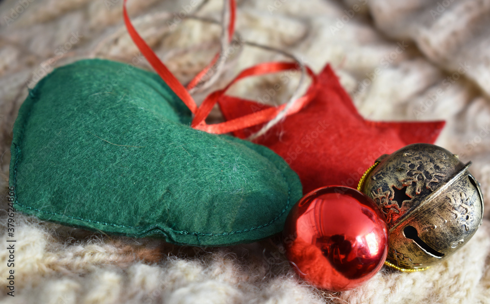 Naklejka premium Grünes Herz, Roter Stern, Christbaumkugel und Schelle als weihnachtliche Dekoration auf Schafwoll Pullover mit Zöpfen für Weihnachtskarte, Tischkarte, Geschenkanhänger