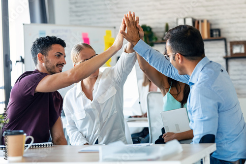 Photos Group of successful smart business team celebrating good job while holding up their right hands on coworking place