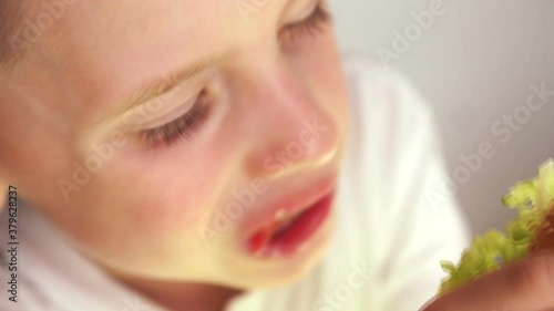 Close-up Caucasian little boy eating appetizing hamburger. Child eating fast food breakfast. Selective focus, shallow depth of field.