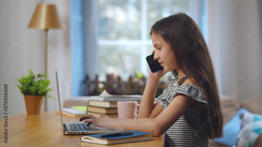 Pretty little girl Studying or Browsing Interest on Laptop while Talking Smartphone Pretty little girl Studying or Browsing Interest on Laptop while Talking Smartphone