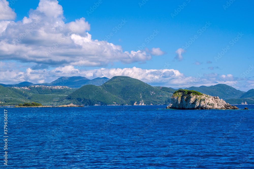 Beautiful landscape - sea lagoon with turquoise water, stones and rocks, blue sky with clouds and mountains on the horizon. Corfu Island, Greece.