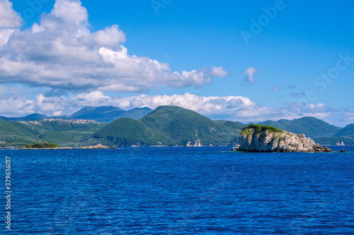 Beautiful landscape - sea lagoon with turquoise water, stones and rocks, blue sky with clouds and mountains on the horizon. Corfu Island, Greece.