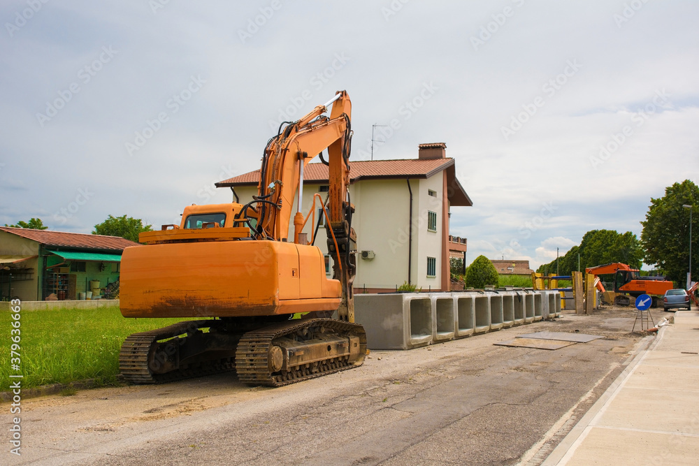 A crawler excavator with a rotating house platform and continuous caterpillar track with some reinforced concrete box culverts. On the site of a sewage system replacement scheme in north west Italy
