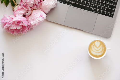 Fototapeta Naklejka Na Ścianę i Meble -  Cropped shot or laptop computer keyboard, cappuccino and the bouquet of peony flowers with a lot of copy space for text on textured table. Close up, top view.