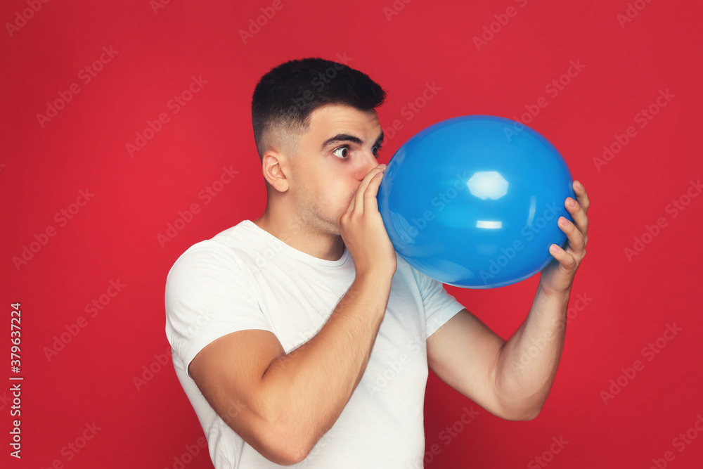 Yuong man blowing balloon on red background Yuong man blowing balloon on red background