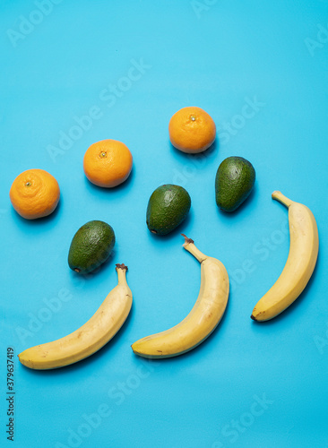 Tangerines, avocado and bananas lie on a blue background