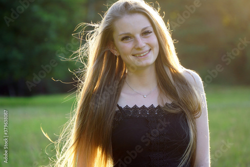 Hübsche junge Frau im Portrait lächelt freundlich an einem sonnigen Sommertag im Park