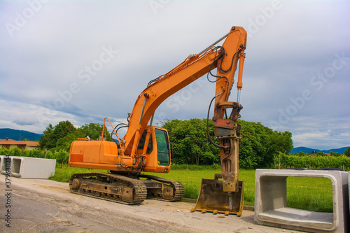 A crawler excavator with a rotating house platform and continuous caterpillar track with some reinforced concrete box culverts. On the site of a sewage system replacement scheme in north west Italy 