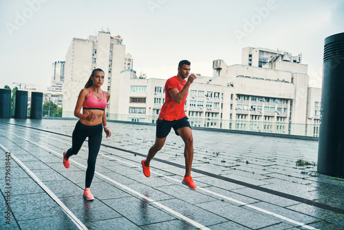 Full length of two young people in sports clothing jogging outdoors together
