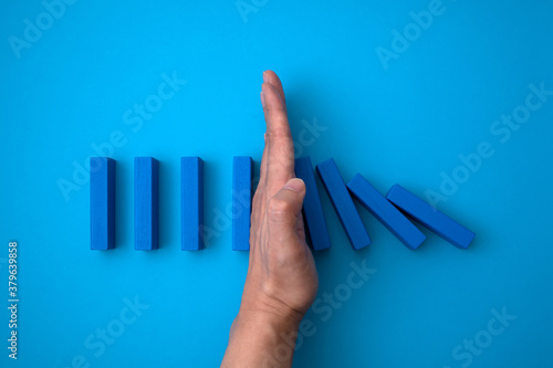 blue domino blocks that begins to fall and a hand that prevents it from falling.