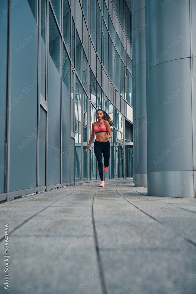 Full length of attractive young woman in sports clothing jogging while exercising outdoors Full length of attractive young woman in sports clothing jogging while exercising outdoors