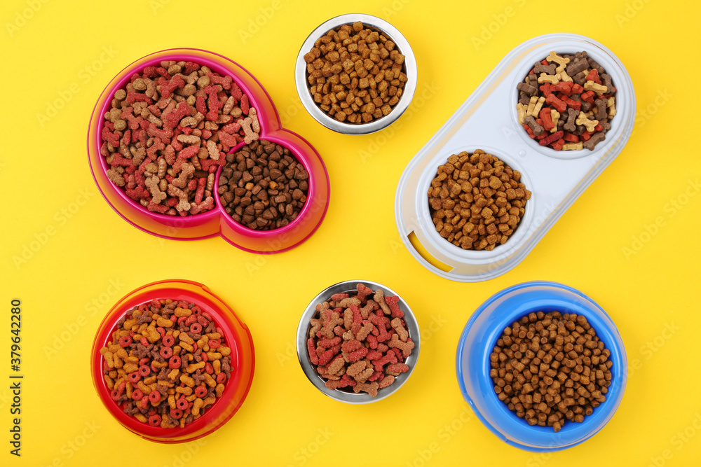 Dry pet food in bowls on yellow background
