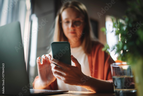 Woman sitting in a coworking space using phone ordering food for lunch online via the Internet application, focus on cellphone, Young millennial girl typing message in social network