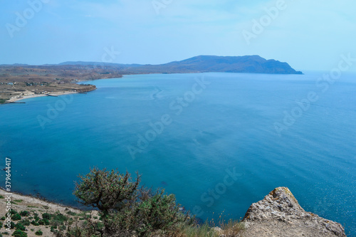 view of beautiful coast with green trees of bay of sea with blue water among hills and high mountains. Crimea, Russia, summer sunny landscape