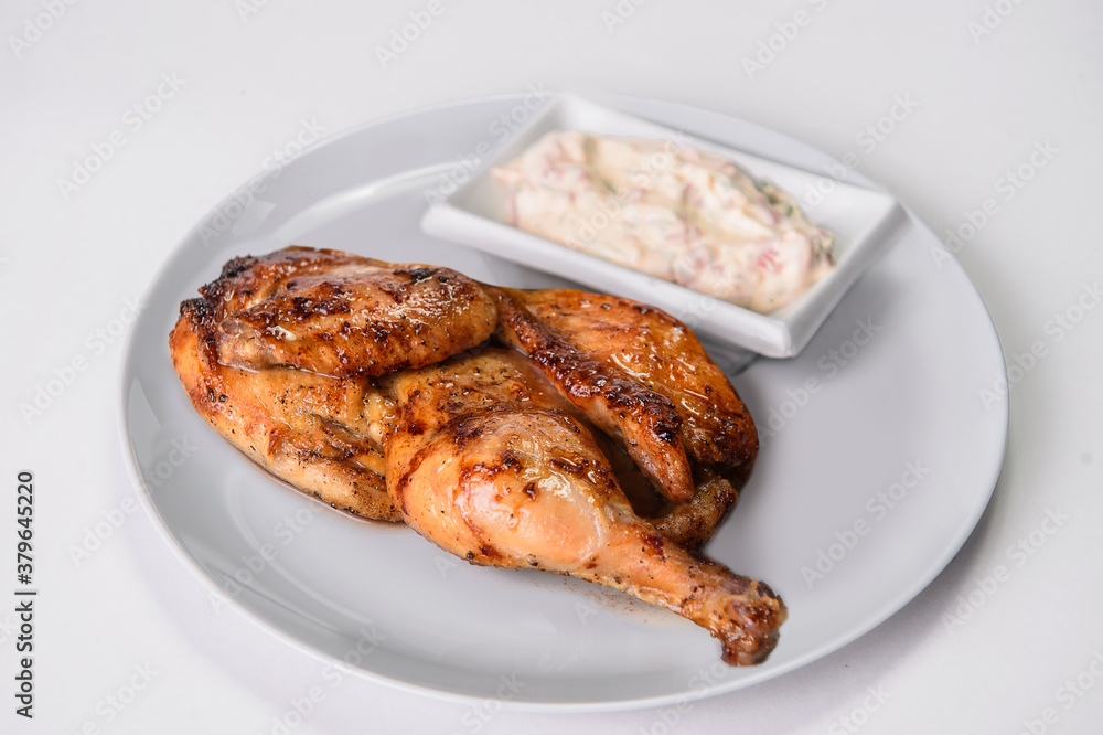 Half of Grilled chicken Tabaka on gray plate isolated on background served with sauce in white bowl. Georgian cuisine. Restaurant menu food isolation 
