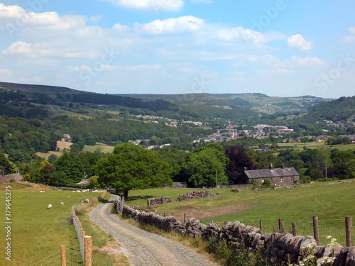 country lane running downhill surrounded by fields with sheep with a view of the town of mytholmroyd surrounded by woods and fields in the calder valley west yorkshire photo