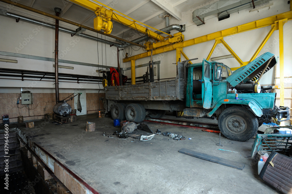 At the car mechanic workshop. Very old truck being repaired, vehicle inspection pit, hoist and engine disassembled