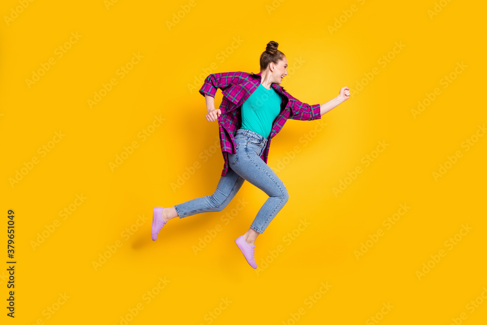 Full body profile photo of attractive teen lady jump high up run race marathon excited to win rushing competition wear casual plaid shirt sneakers jeans isolated yellow color background