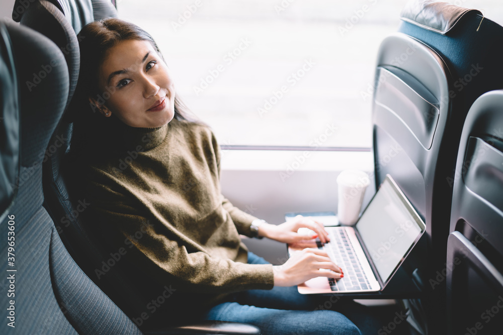 Fototapeta premium Satisfied young woman using laptop in train