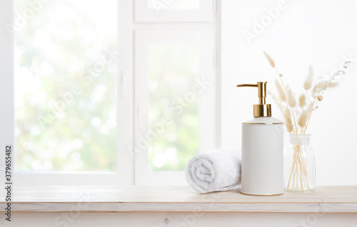 Towel and soap dispenser on table against blurred window background