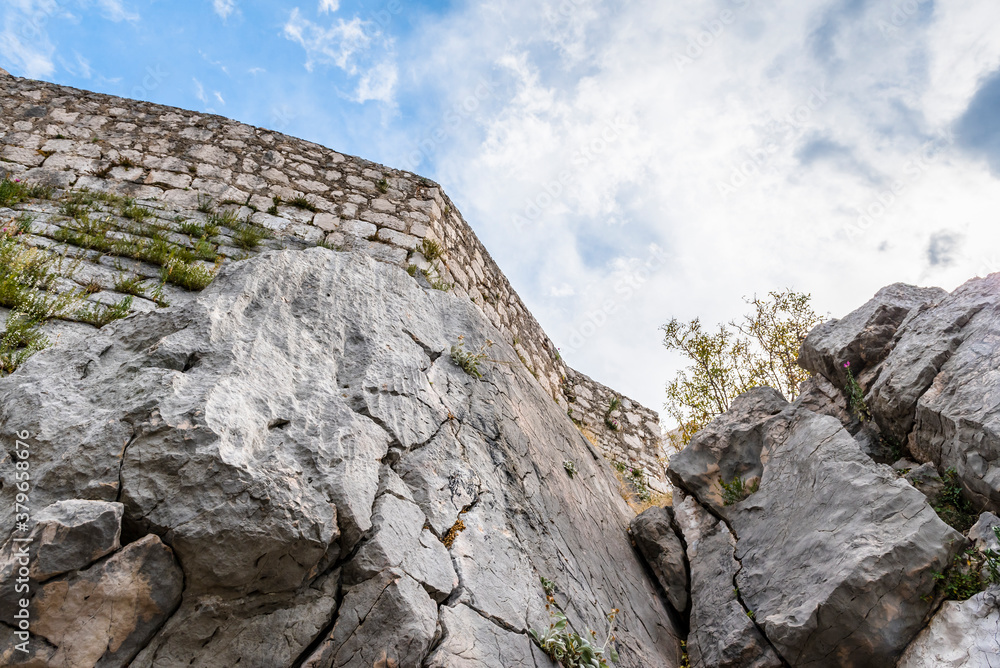 Naklejka premium Bottom view of the rock and wall of a medieval fortress against a cloudy sky in Sibenik, Croatia