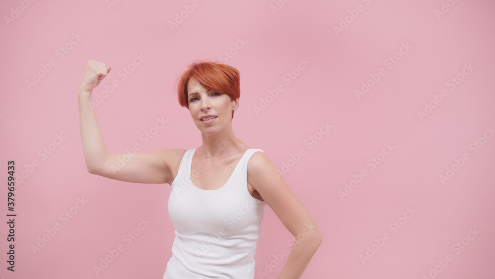 Beautiful excited middle aged redhead woman flexing her muscles, isolated on pink purple background. High quality photo Beautiful excited middle aged redhead woman flexing her muscles, isolated on pink purple background. High quality photo