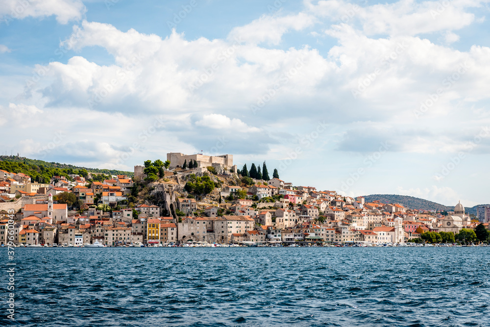 Sea view of the town of Sibenik, Croatia, with a medieval fortress on a hill against the sky with clouds