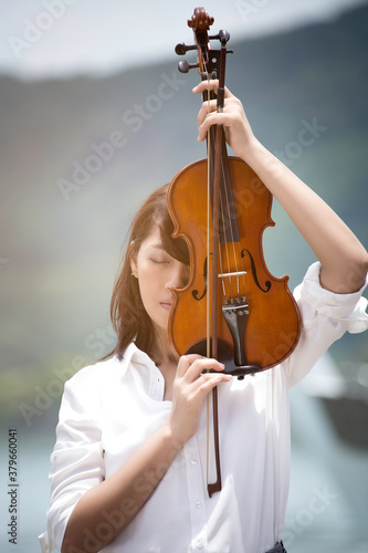 Beautiful asian woman hold violin on nature background, in emotion feeling happy.