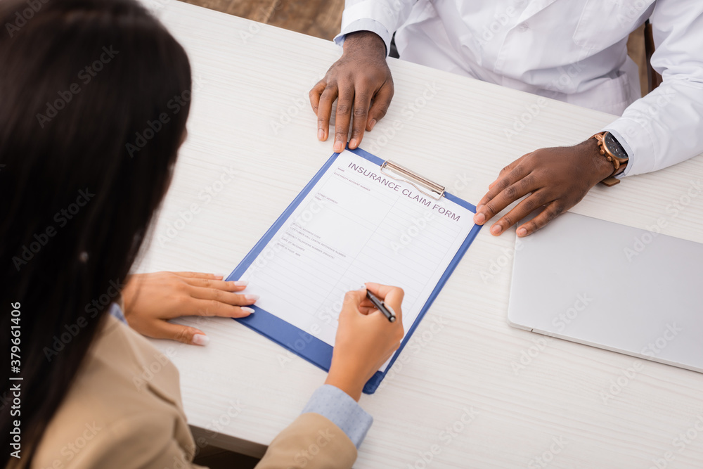 overhead view of patient signing insurance claim form near african american doctor overhead view of patient signing insurance claim form near african american doctor