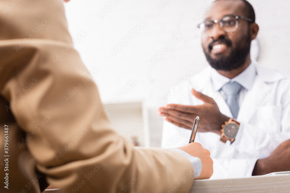 Obraz premium selective focus of bearded african american doctor in eyeglasses pointing with hand near patient