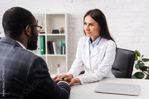 selective focus of brunette doctor touching hands of african american man in clinic