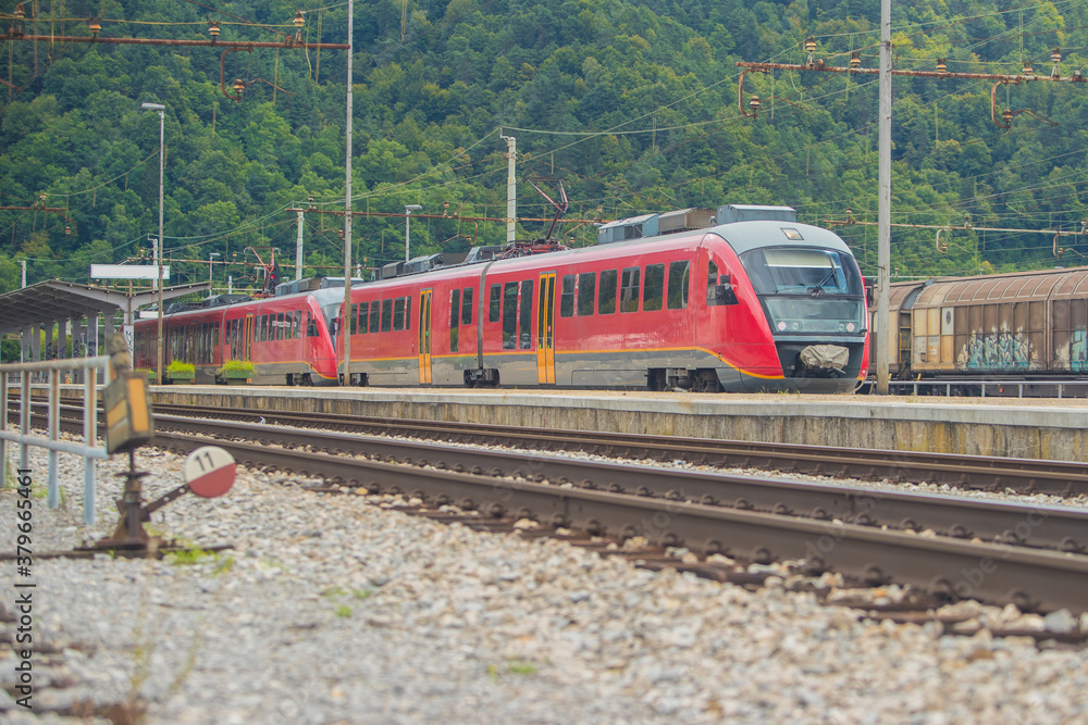 Modern electrical multiple unit train on track on a suburban station. Commuter train rushing towards the city in a suburban environment on a sunny day. Modern electrical multiple unit train on track on a suburban station. Commuter train rushing towards the city in a suburban environment on a sunny day.