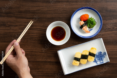 Sushi set and Hand holding chopsticks on wooden background, top view. 