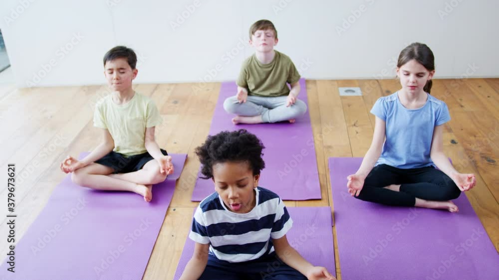 Group of children sitting on exercise mats and meditating in yoga studio - shot in slow motion Group of children sitting on exercise mats and meditating in yoga studio - shot in slow motion