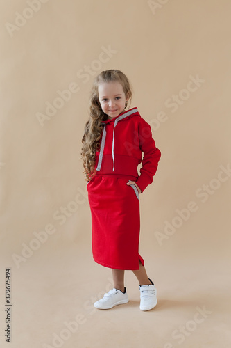 A little girl in a red suit poses on a colored background. Fashionable children's clothing.