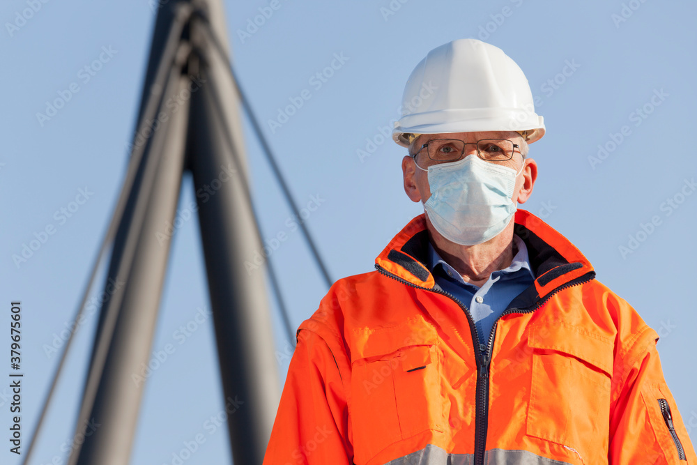 Architect or engineer wearing a face mask and protective clothing in front of a industrial background