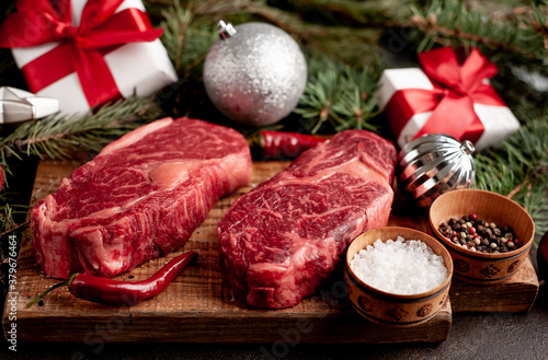 Raw ribeye beef steaks for preparing a dinner for two for a Christmas holiday on a stone table with a Christmas tree and Christmas tree decorations 