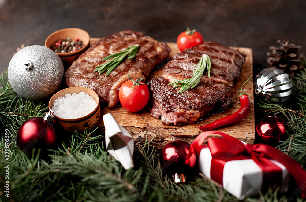 Christmas dinner for two, grilled beef steak ribeye, herbs and spices on a stone table with a Christmas tree and New Year's toys Christmas dinner for two, grilled beef steak ribeye, herbs and spices on a stone table with a Christmas tree and New Year's toys