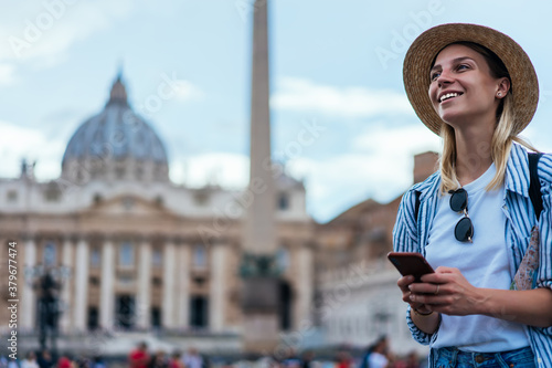 Canvas Print Happy female tourist in straw hat holding mobile technology and smiling during s