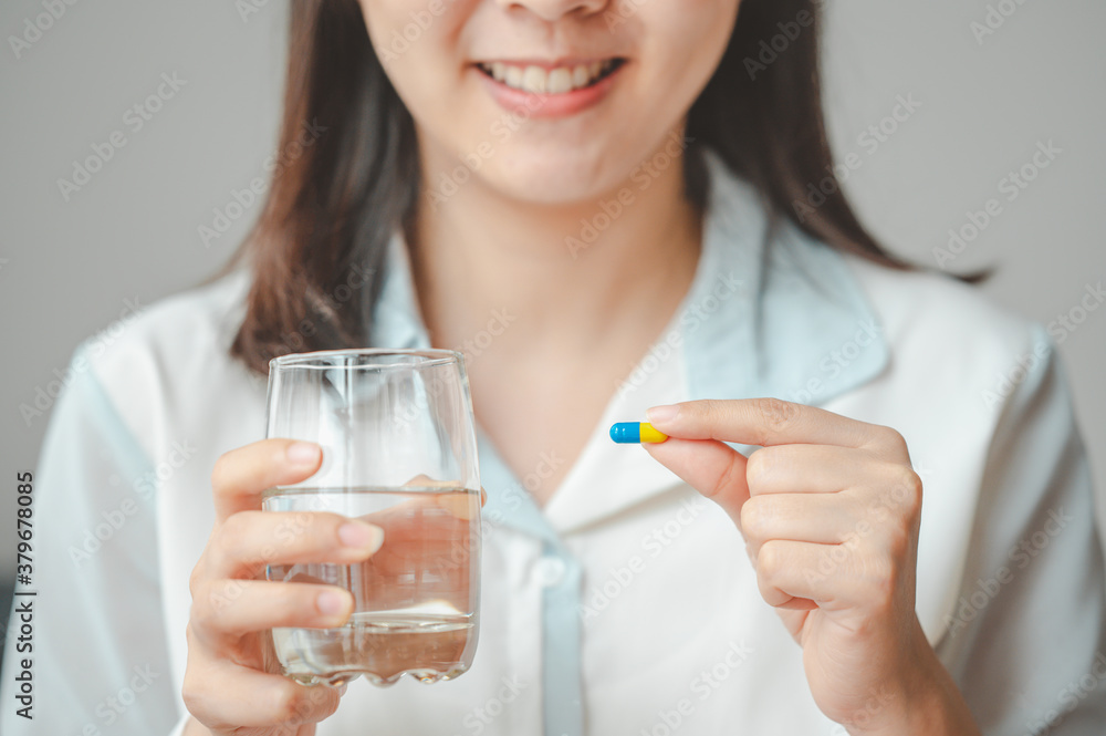 Close up shot of smiling woman holding capsule pill and glass of water. Image focused on capsule Close up shot of smiling woman holding capsule pill and glass of water. Image focused on capsule