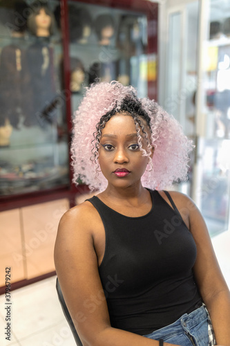 Beautiful black girl sitting in a hairdressing shop with pink crochet styl hair.