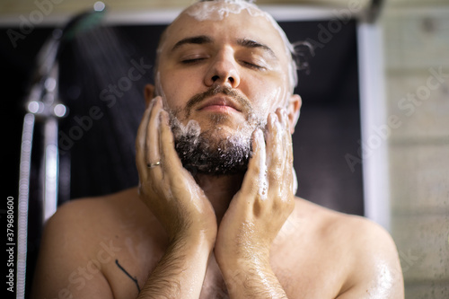 Close up view of handsome man with closed eyes washing beard in bathroom, taking shower. Lifestyle, beauty, personal care, relaxing time, young guy enjoying showering, Body, skin, hair hygiene