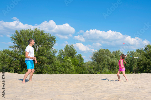 Sports family games on the beach. Father and daughter play beach badminton. Sports, recreation, vacations, active lifestyle concept.