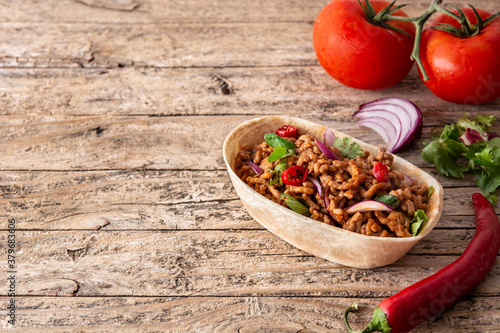 Mexican barquita taco with beef, chilli, tomato, onion and spices on wooden table 