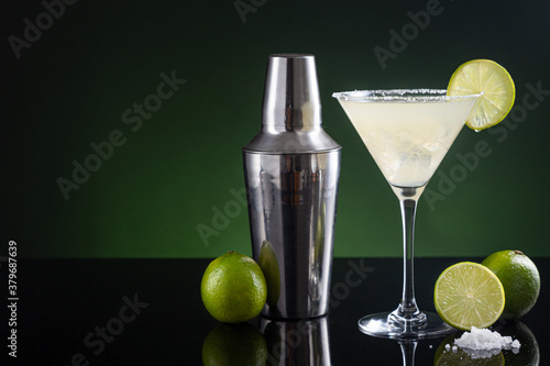 Typical Mexican margarita cocktail with lime slice ice and cocktail shaker on black and green background. with copy space