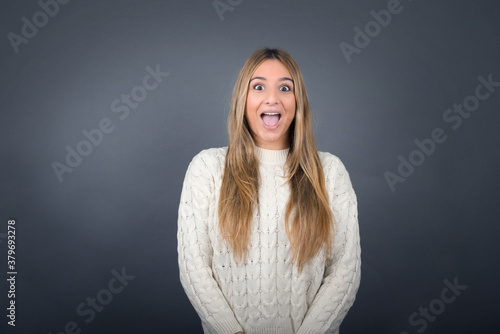 Beautiful blonde young woman wearing white sweater feeling confident against gray studio background.